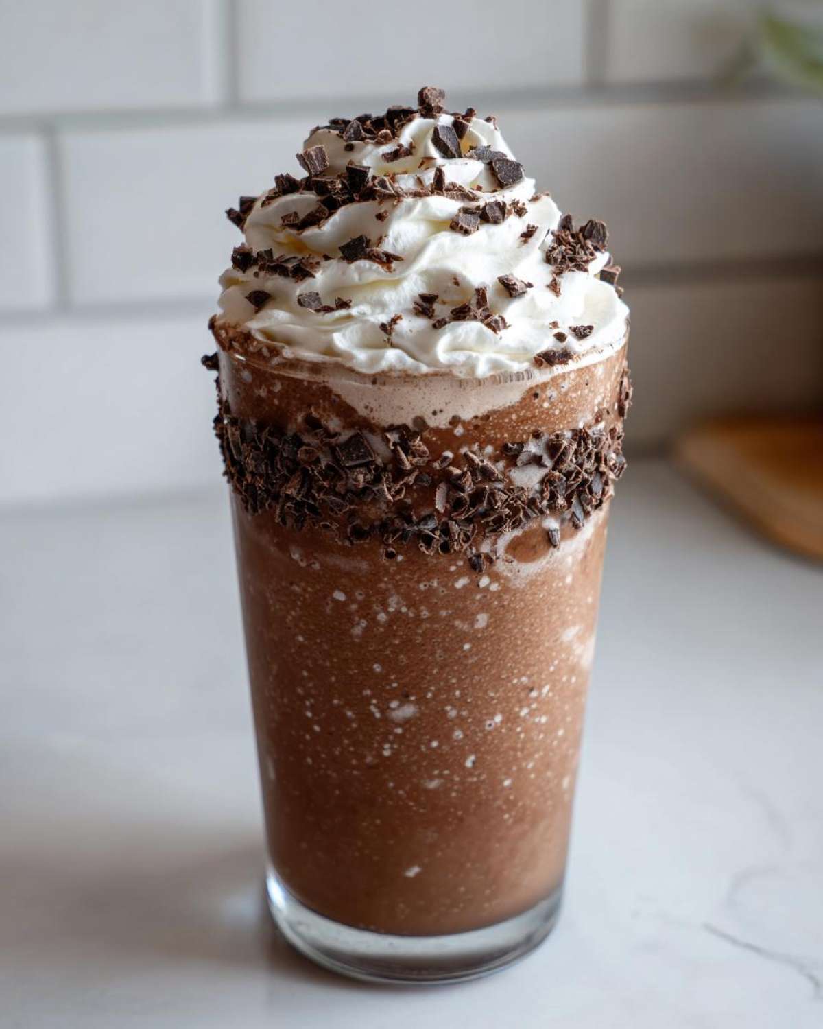 A tall glass filled with rich, blended frozen hot chocolate, topped with whipped cream and chocolate shavings.