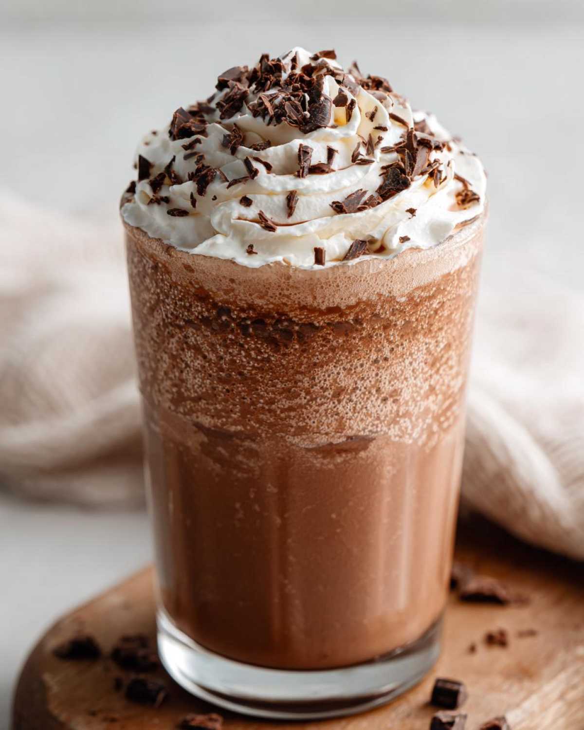 A tall glass filled with thick, blended frozen hot chocolate topped with whipped cream and chocolate shavings.