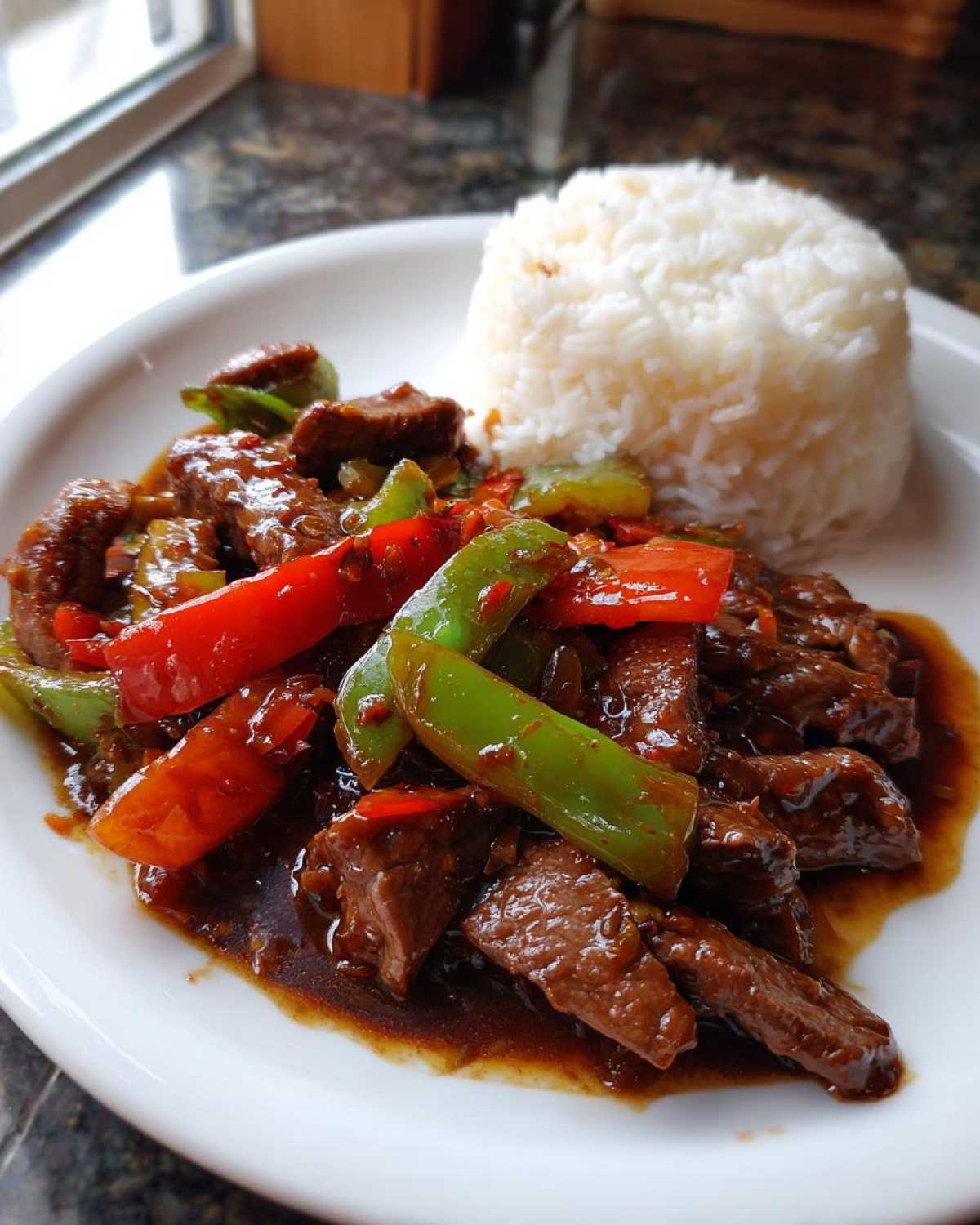 A plate featuring savory pepper steak stir-fry with green and red bell peppers next to a mound of white rice.