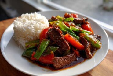 A plate featuring savory pepper steak stir-fry with red peppers and green onions, served alongside a mound of white rice.