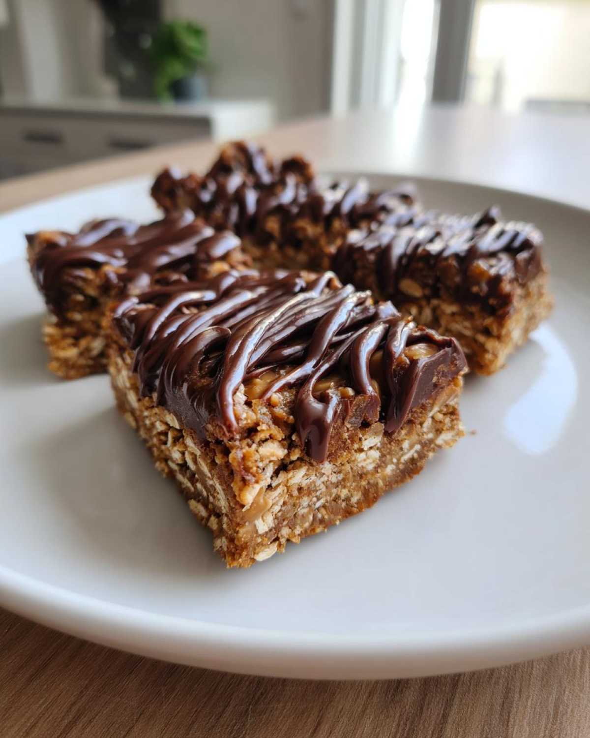 Four homemade protein bars made with oats and topped with a rich, dark chocolate drizzle, served on a white plate.