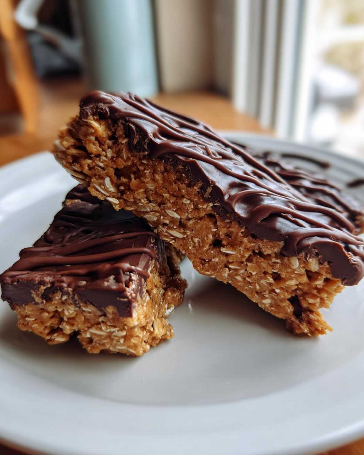 Two stacked, chewy homemade protein bars topped with melted, drizzled dark chocolate, resting on a white plate.
