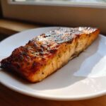 A beautifully glazed, seasoned fillet of air fryer salmon resting on a white plate.