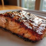 Close-up of a perfectly cooked, glazed air fryer salmon fillet on a white plate.