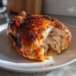 A perfectly cooked air fryer whole chicken resting on a white plate, showing juicy, shredded white meat exposed.