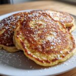 Close-up of fluffy almond flour pancakes stacked on a white plate, generously dusted with powdered sugar.