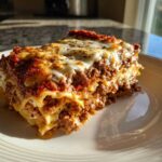 A thick, cheesy slice of homemade lasagna with rich meat sauce layers, served on a white plate.