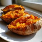 Close-up of fluffy, orange baked sweet potato halves seasoned with black pepper on a white plate.