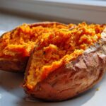 Close-up of a perfectly baked sweet potato cut in half, showing fluffy, bright orange flesh.
