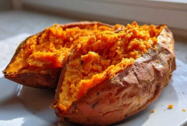 Close-up of a perfectly baked sweet potato cut in half, showing fluffy, bright orange flesh.