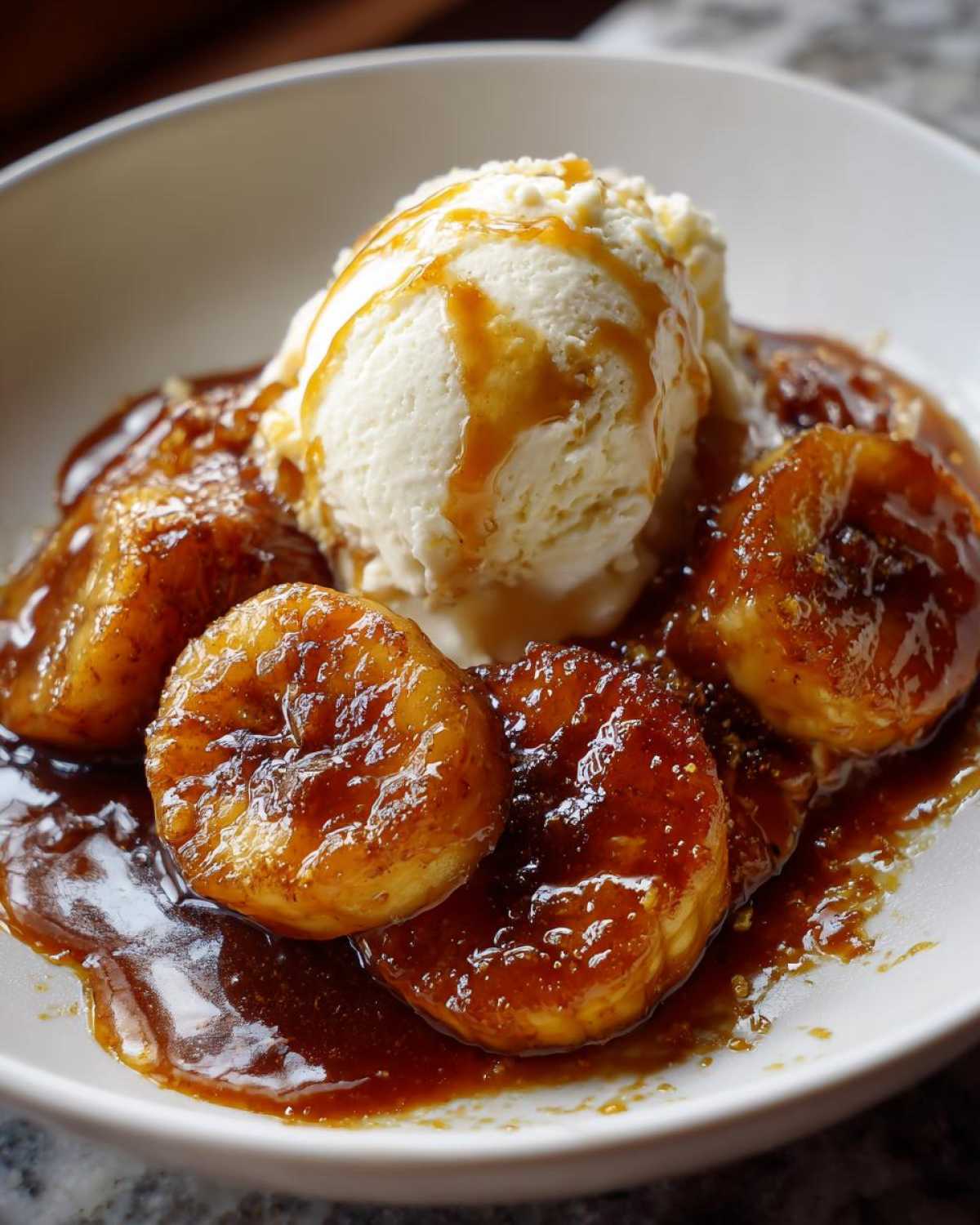 Close-up of warm, caramelized bananas foster topped with a scoop of vanilla ice cream drizzled with caramel sauce.