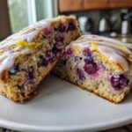 Two halves of a moist blueberry scone, showing the interior packed with blueberries and topped with lemon glaze.