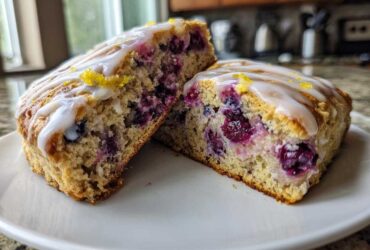 Two halves of a moist blueberry scone, showing the interior packed with blueberries and topped with lemon glaze.