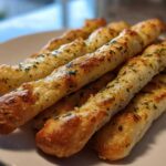 Close-up of several golden brown, cheesy breadsticks topped with parsley on a white plate.