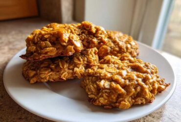 Close-up of four moist, orange-hued breakfast cookie oat treats stacked and resting on a white plate.