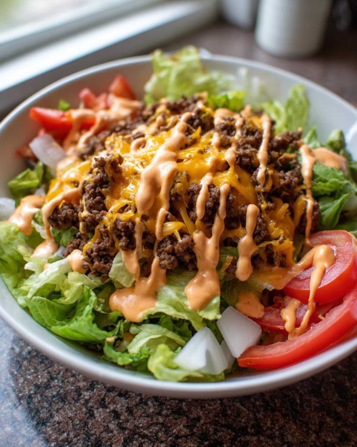 A close-up of an amazing cheeseburger bowl featuring seasoned ground beef, melted cheese, lettuce, tomatoes, and special sauce.