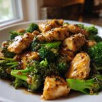Close-up of glossy, saucy chicken and broccoli stir-fry topped with black and white sesame seeds.