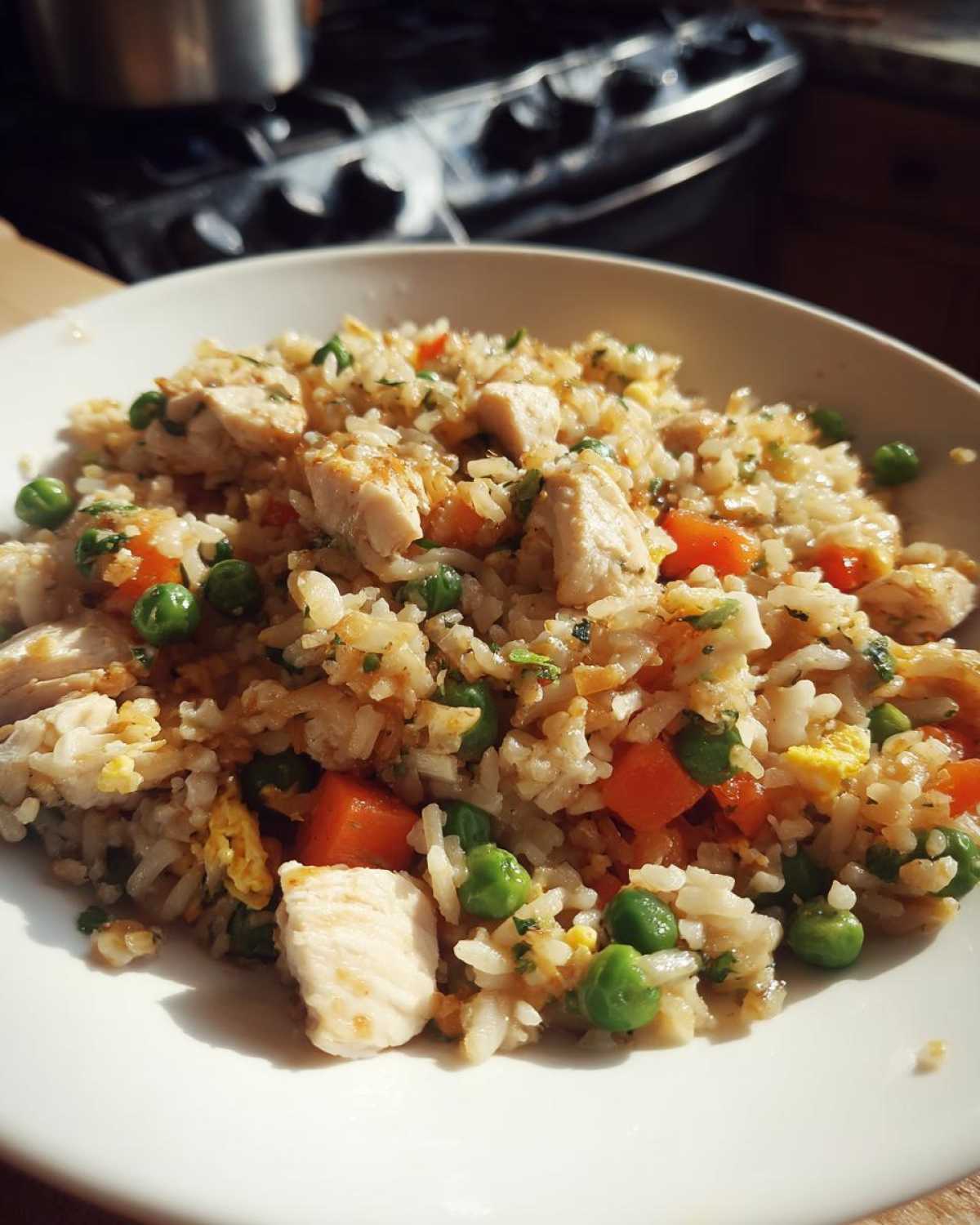 Close-up of a white bowl filled with amazing chicken fried rice, featuring white chicken pieces, green peas, and diced carrots.