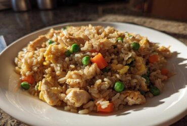 A close-up of a plate of amazing chicken fried rice featuring rice, chicken pieces, carrots, peas, and scrambled egg.