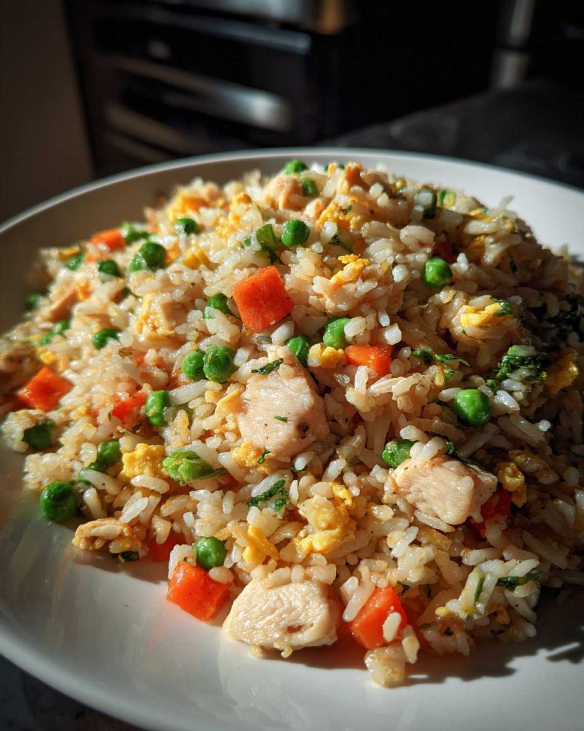 A close-up, sunlit plate of amazing chicken fried rice mixed with scrambled egg, bright green peas, and diced carrots.