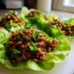 Close-up of several fresh chicken lettuce wraps filled with savory ground chicken and topped with green onions.