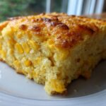 Close-up of a moist slice of cornbread casserole, studded with whole corn kernels and featuring a golden, slightly browned top.