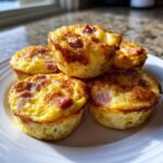 A stack of five golden brown, baked ham and cheese egg bites resting on a white plate.
