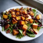 Close-up of a vibrant fall harvest salad featuring roasted squash, pecans, dried cranberries, and apple slices on mixed greens.