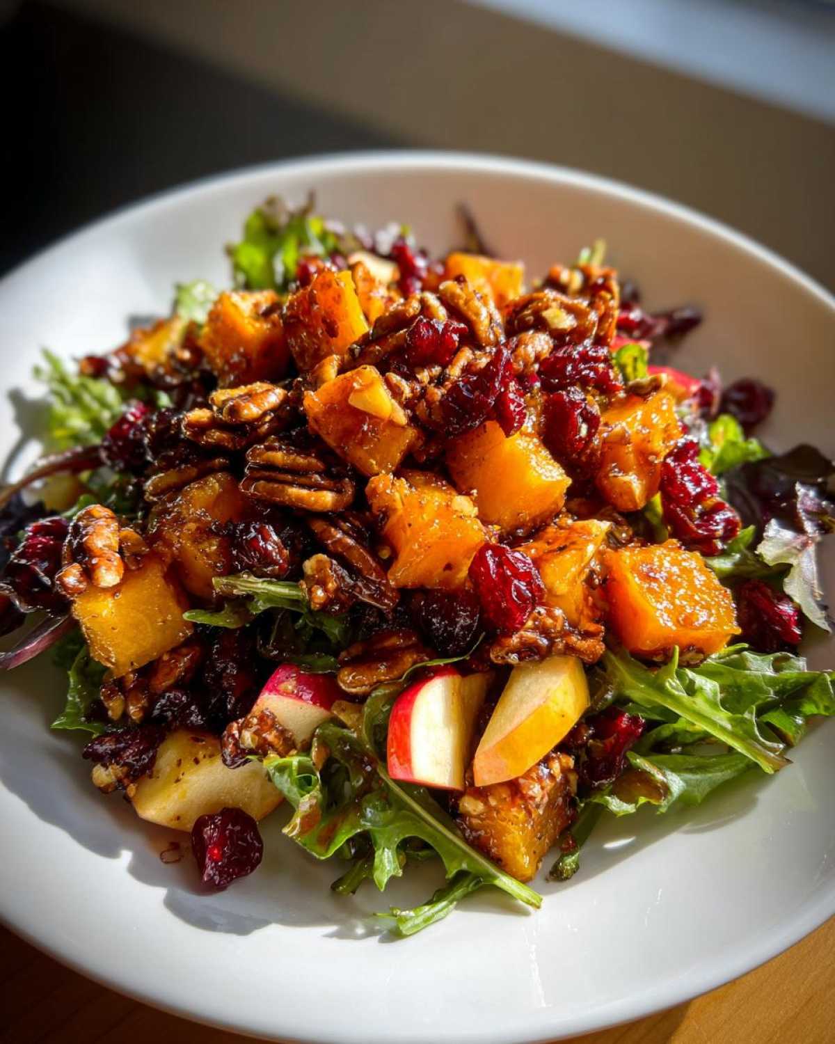 A vibrant fall harvest salad featuring roasted squash, pecans, dried cranberries, and apple slices over mixed greens.