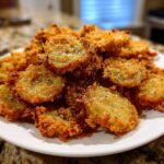 A generous pile of golden brown, crispy Fried Pickles seasoned with herbs and salt on a white plate.