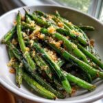 Close-up of bright green beans tossed with toasted garlic breadcrumbs in a white bowl.