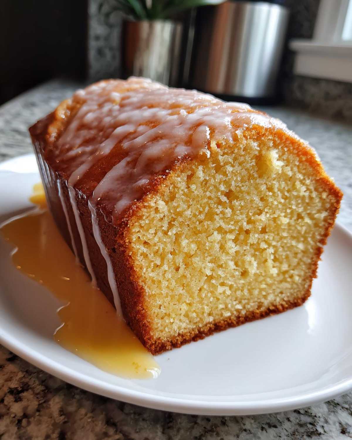 Close-up of a moist slice of lemon pound cake topped with white glaze and extra syrup.