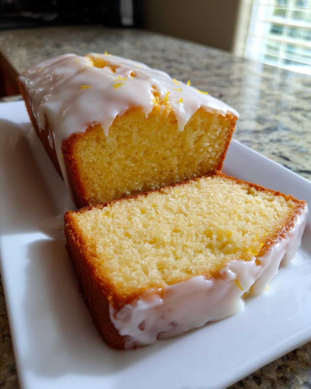 A slice cut from a loaf of amazing lemon pound cake topped with thick white glaze and lemon zest.