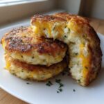 A stack of golden brown mashed potato cakes, one cut open to show melted cheddar cheese inside.