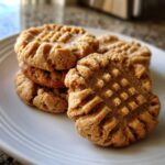 A close-up stack of freshly baked peanut butter cookies showing the classic crisscross fork marks.