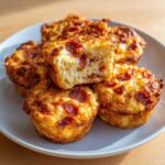 A stack of golden brown, cheesy Pizza Muffins with visible pepperoni pieces, one muffin cut open to show the fluffy interior.