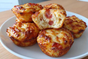 A stack of golden brown pizza muffins with melted, bubbly cheese topping, one is broken open showing pepperoni.