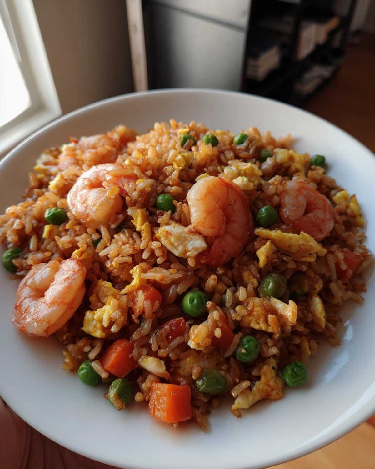 A close-up of a white bowl filled with amazing shrimp fried rice, featuring large pink shrimp, scrambled egg, peas, and diced carrots.