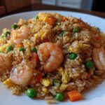 A close-up view of a serving of amazing shrimp fried rice mixed with peas, carrots, and scrambled egg.