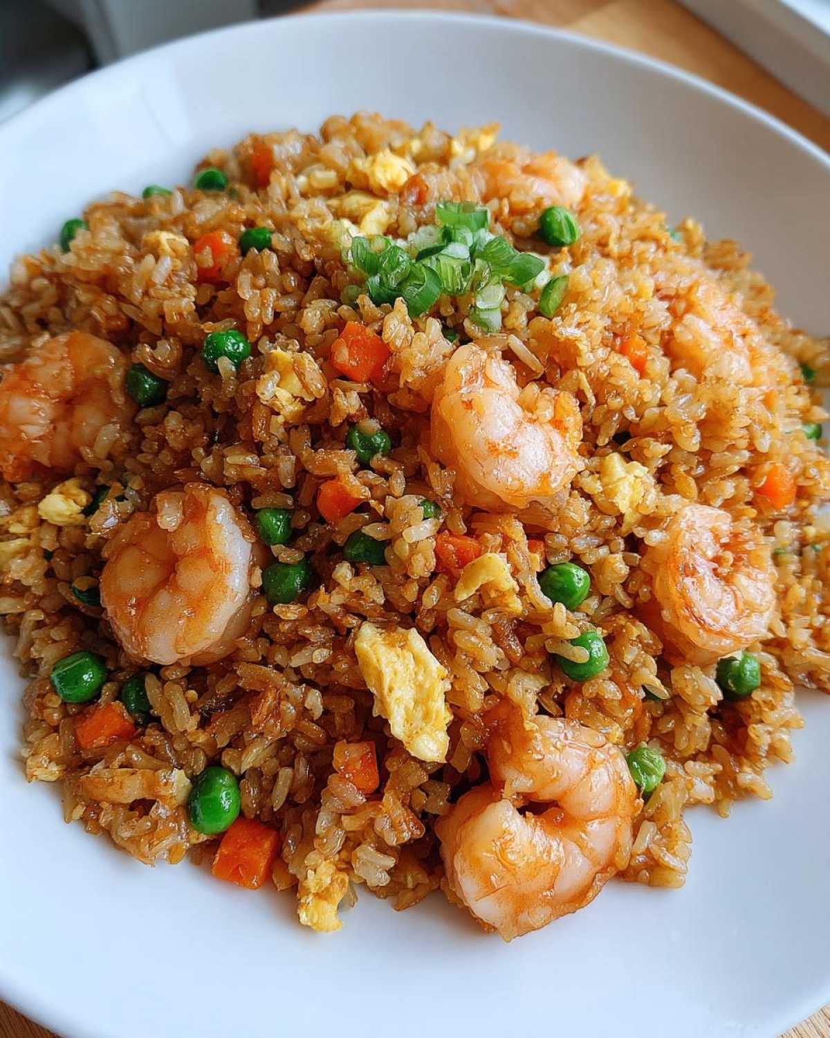 Close-up of a heaping serving of amazing shrimp fried rice with visible shrimp, peas, carrots, and scrambled egg.
