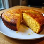 Close-up of a golden brown skillet cornbread, with one slice cut out showing the moist interior texture.