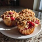 Three homemade strawberry muffins topped with a generous brown sugar streusel sitting on a white plate.