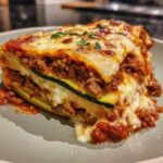 A generous slice of zucchini lasagna layered with meat sauce and melted cheese, garnished with parsley.