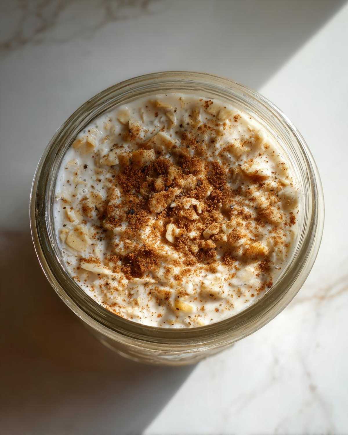 Overhead close-up of apple cinnamon overnight oats in a glass jar, topped with cinnamon and brown sugar.