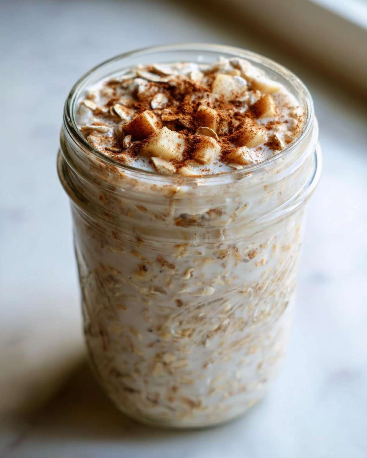 Close-up of apple cinnamon overnight oats in a glass jar, topped with diced apples and cinnamon.
