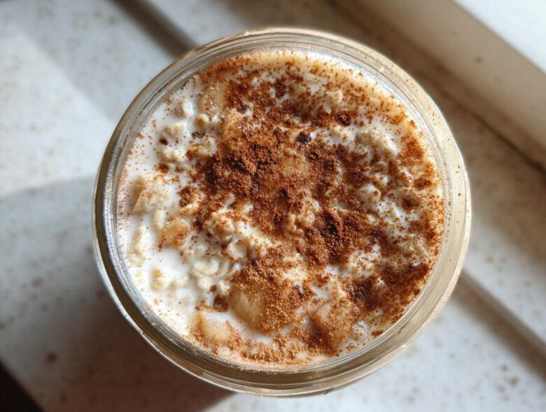 Overhead shot of apple cinnamon overnight oats in a glass jar, topped generously with ground cinnamon.