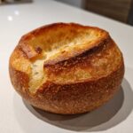 A freshly baked, golden-brown bread bowl with the top sliced open, ready to be filled.