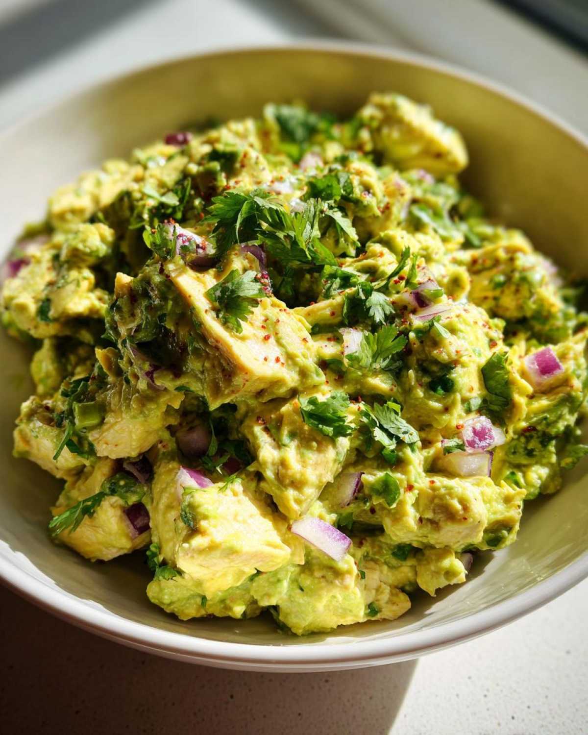 Close-up of a bowl filled with creamy avocado chicken salad, topped with fresh cilantro and red onion.