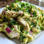 Close-up of creamy avocado chicken salad featuring shredded chicken, diced red onion, and fresh cilantro.