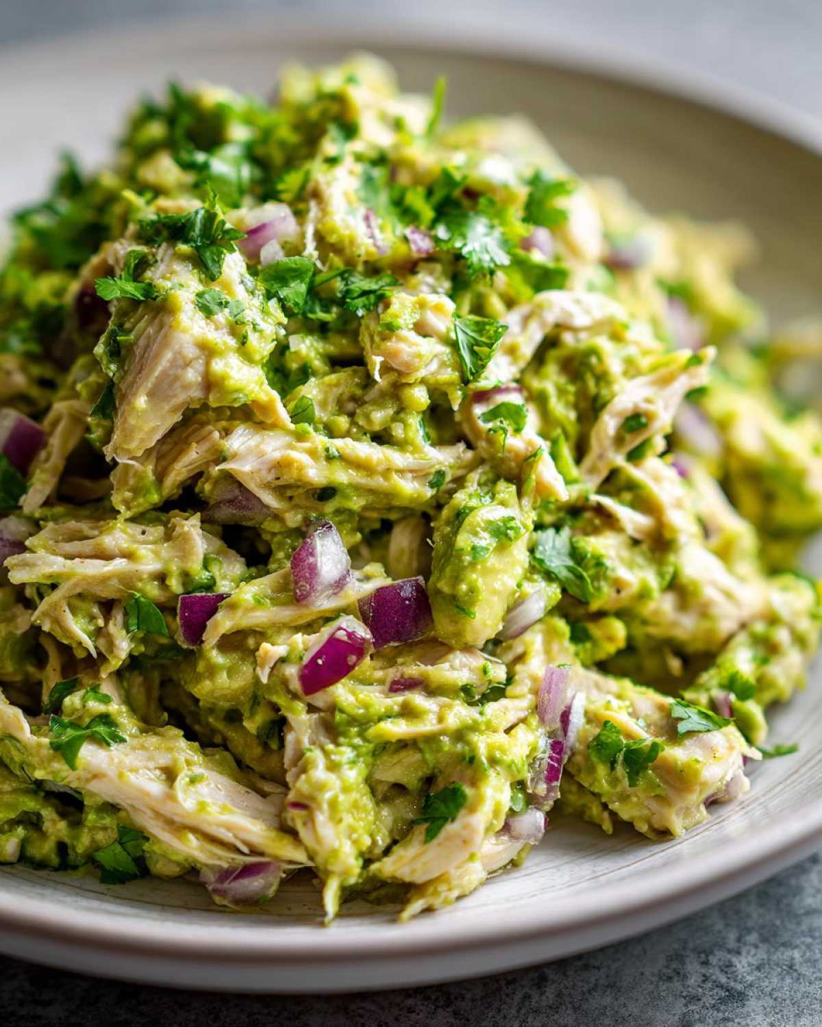 Close-up of creamy avocado chicken salad mixed with chunks of red onion and fresh cilantro.